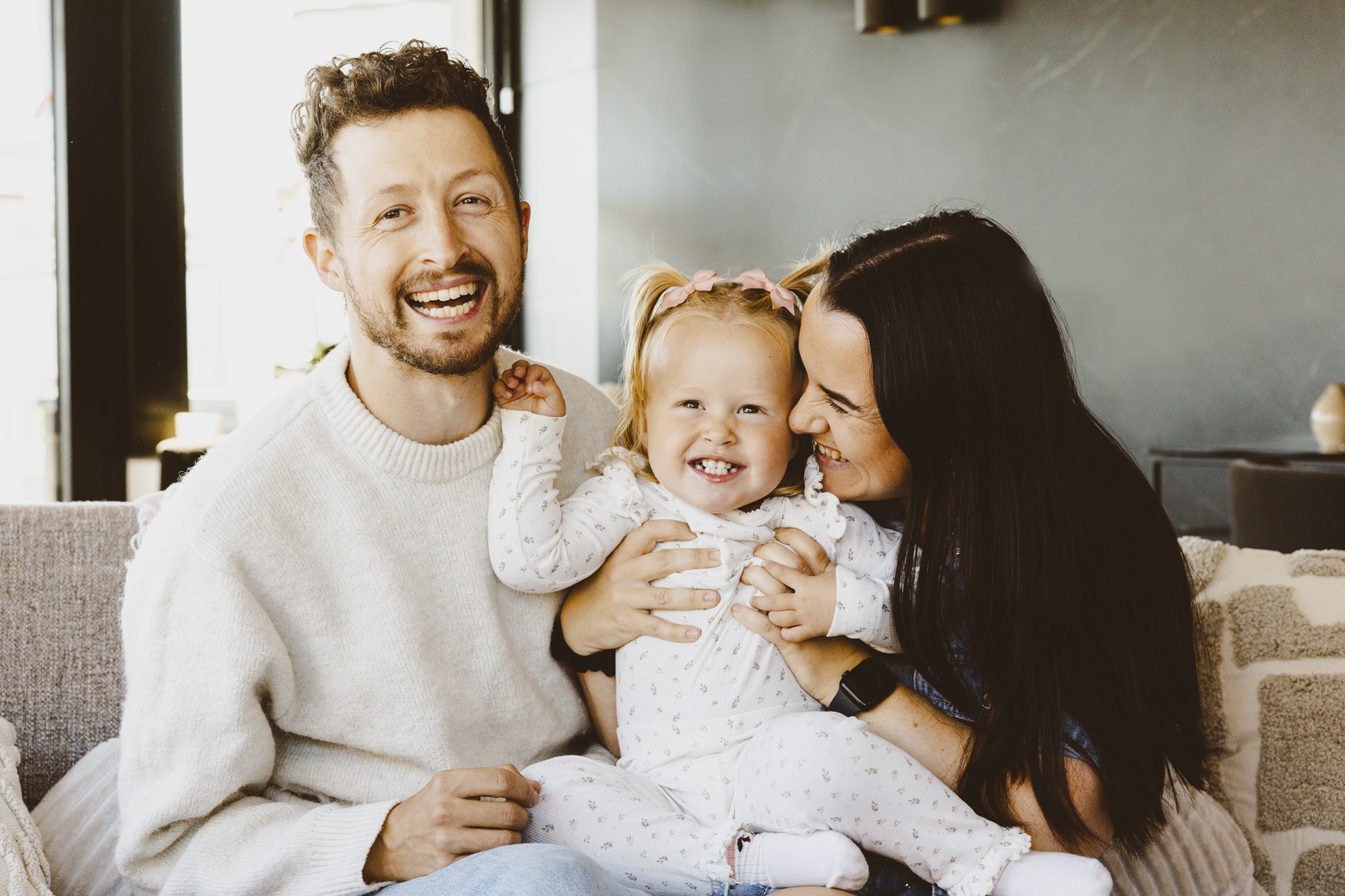 En smilende mann og kvinne sitter med en smilende liten jente på fanget mellom seg.
