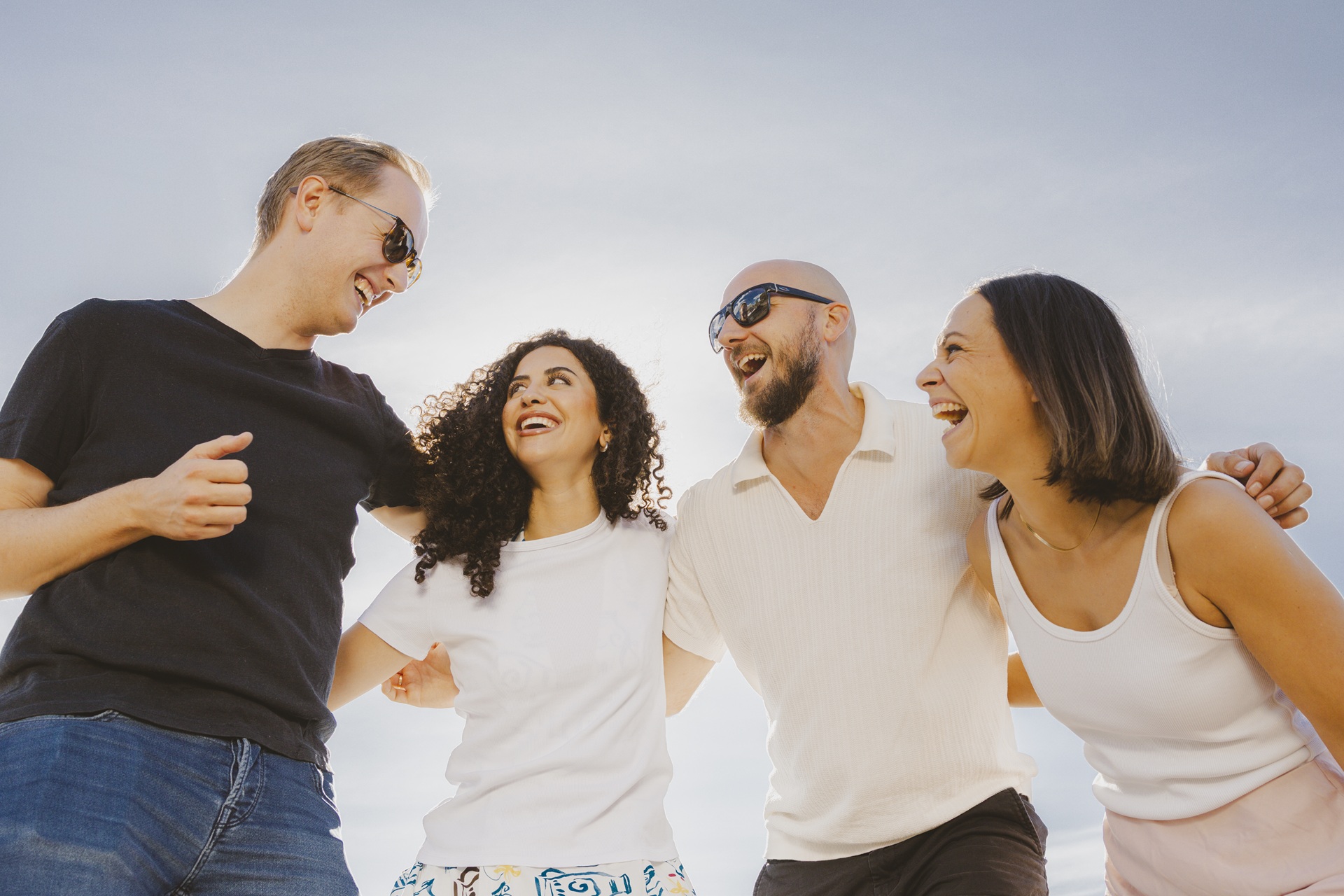 Fire smilende personer står med armene rundt hverandre utendørs under en klar himmel.