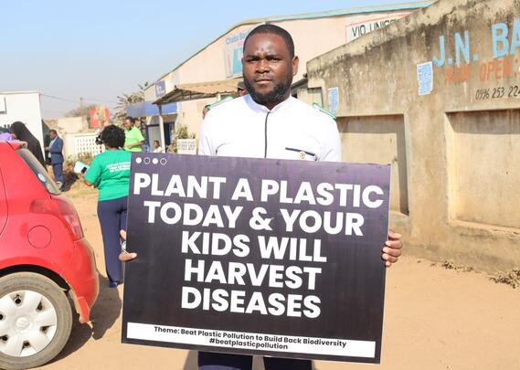 Et medlem av det malawiske sykepleierforbundet i sykepleieruniform som holder en plakat mot forsøpling med plast