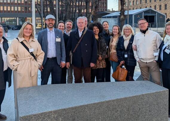 13 mennesker står oppstilt og smiler til kamera. Noen er delvis skjult bak andre.