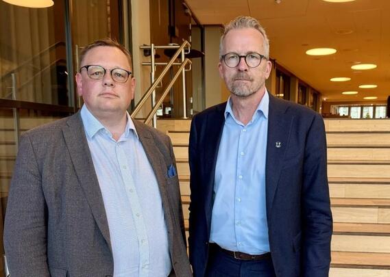 To menn med briller og dress står ved siden av hverandre