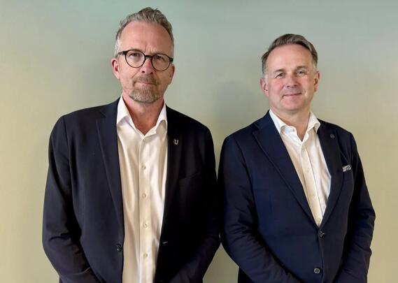 To menn i dress står ved siden av hverandre og ser mot fotografen.