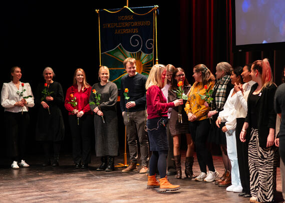 Nominerte under Fylkesmedlemsmøtet 2025 mottar roser på scenen foran NSF Akershus' fane.