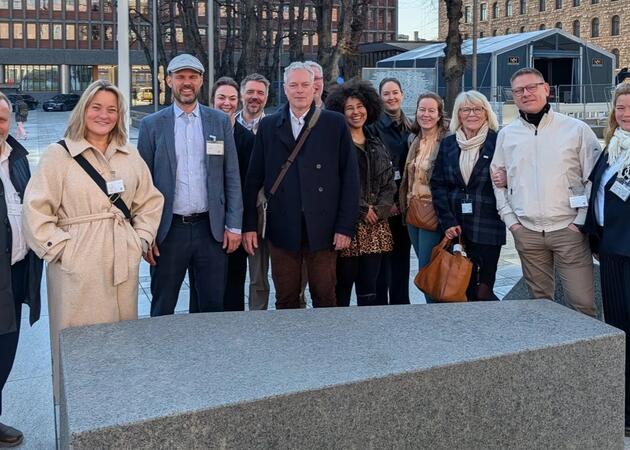 13 mennesker står oppstilt og smiler til kamera. Noen er delvis skjult bak andre.