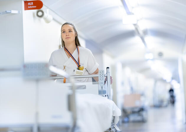 Kvinne som triller på en sykeseng på sykehus, med hvit uniform.