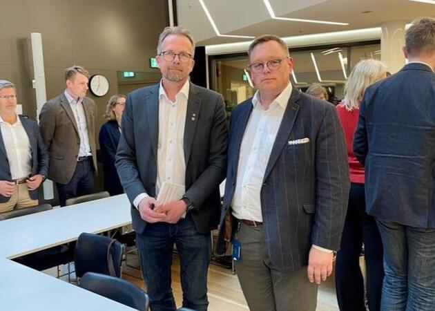To menn i dress står ved siden av hverandre og ser mot fotografen.