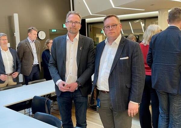To menn i dress står ved siden av hverandre og ser mot fotografen.