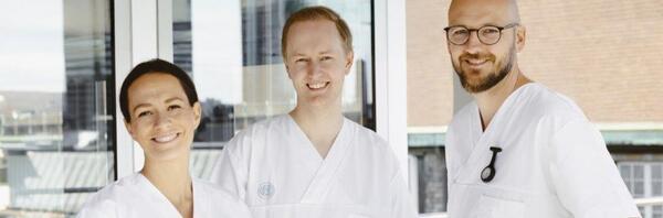 Tre sykepleiere i uniform smiler til kamera