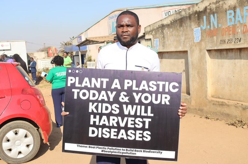 Et medlem av det malawiske sykepleierforbundet i sykepleieruniform som holder en plakat mot forsøpling med plast