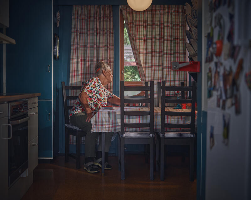 Eldre person sitter på kjøkkenet og titter ut vinduet