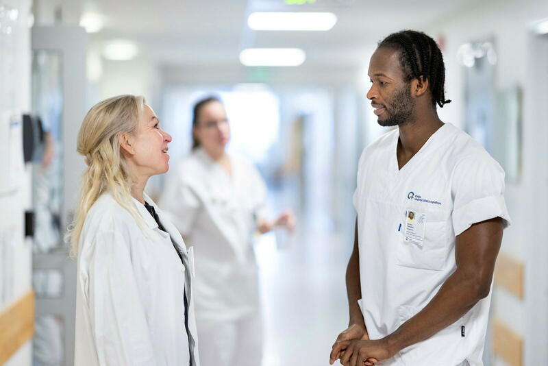 En mann og en dame i hvit sykepleieruniform snakker sammen i en korridor.