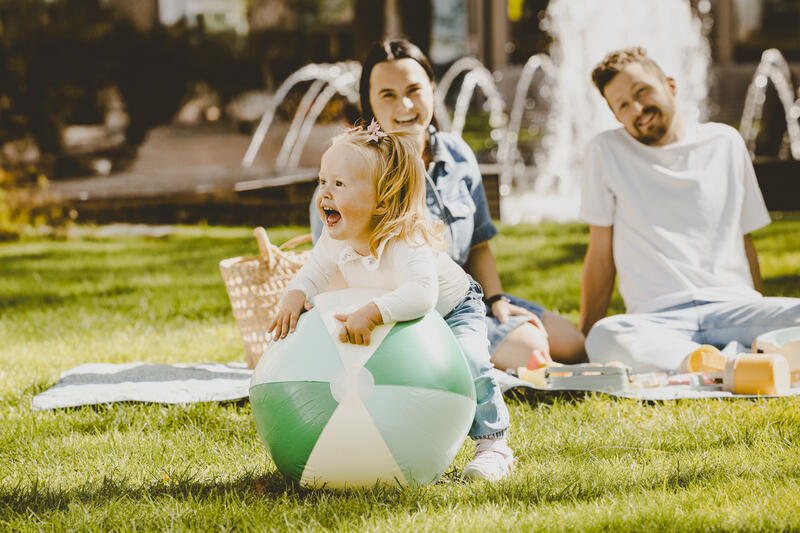 lite barn og badeball med foreldre i bakgrunn