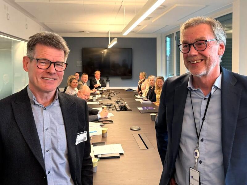 To menn med briller og dress smiler til kameraet.