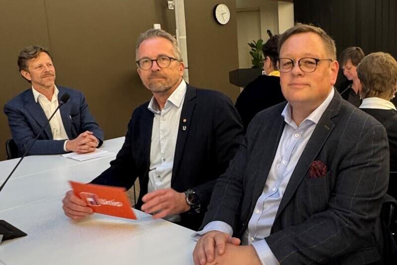 To menn i dress sitter ved siden av hverandre og ser mot fotografen.