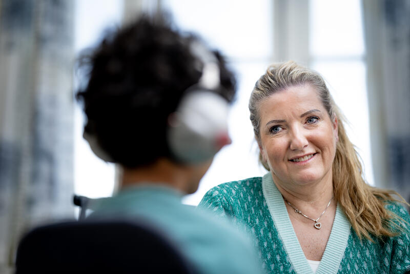 Dame med grønn genser som smiler til et barn med headset