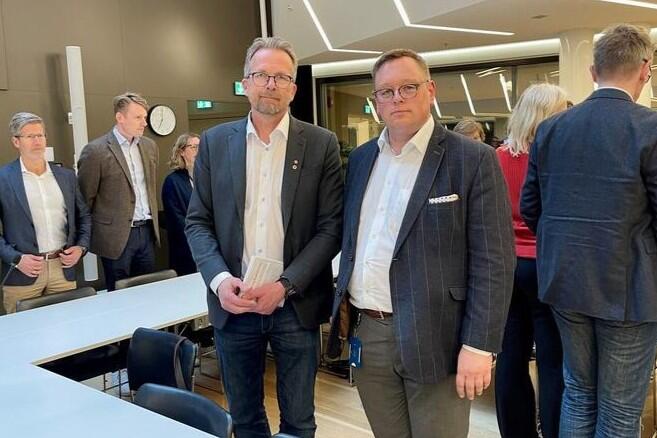 To menn i dress står ved siden av hverandre og ser mot fotografen.
