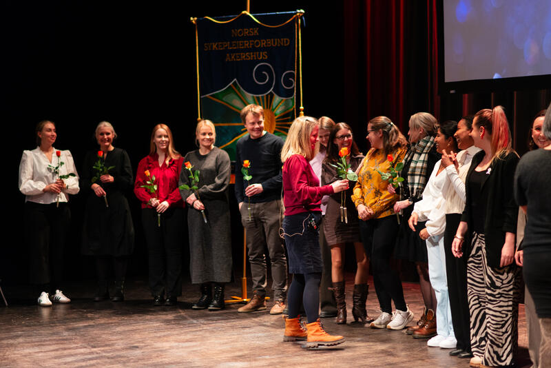 Nominerte under Fylkesmedlemsmøtet 2025 mottar roser på scenen foran NSF Akershus' fane.